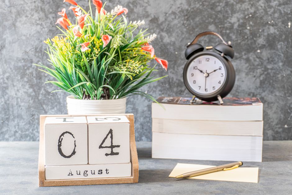 A styled indoor setup featuring a calendar showing August 4 and an alarm clock on books.